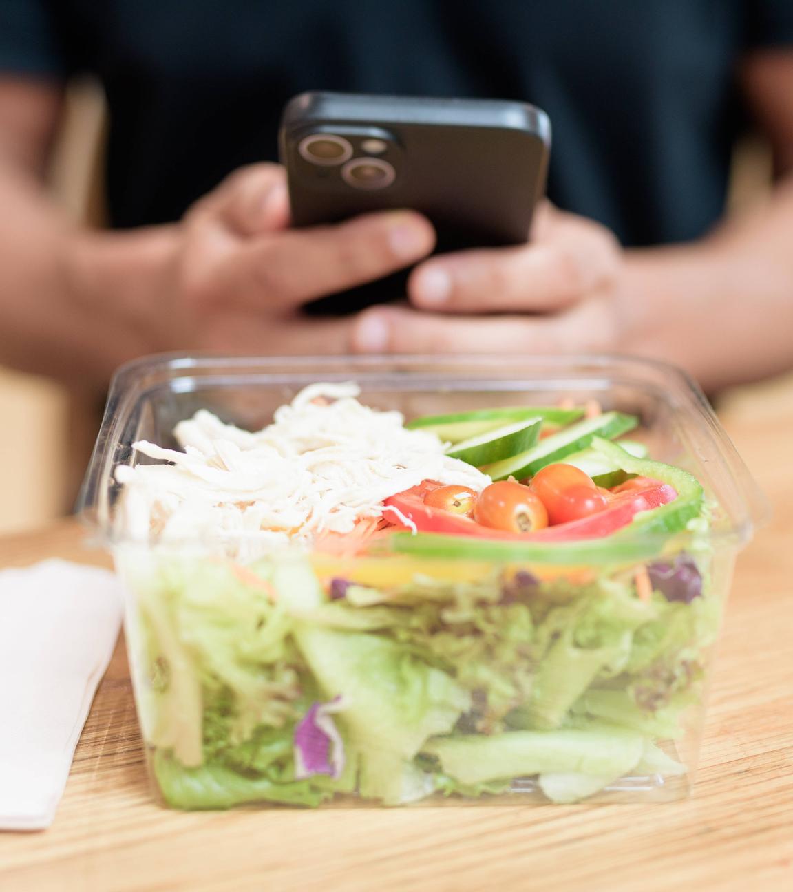 Mann mit Smartphone sitzt vor einer Salatschüssel