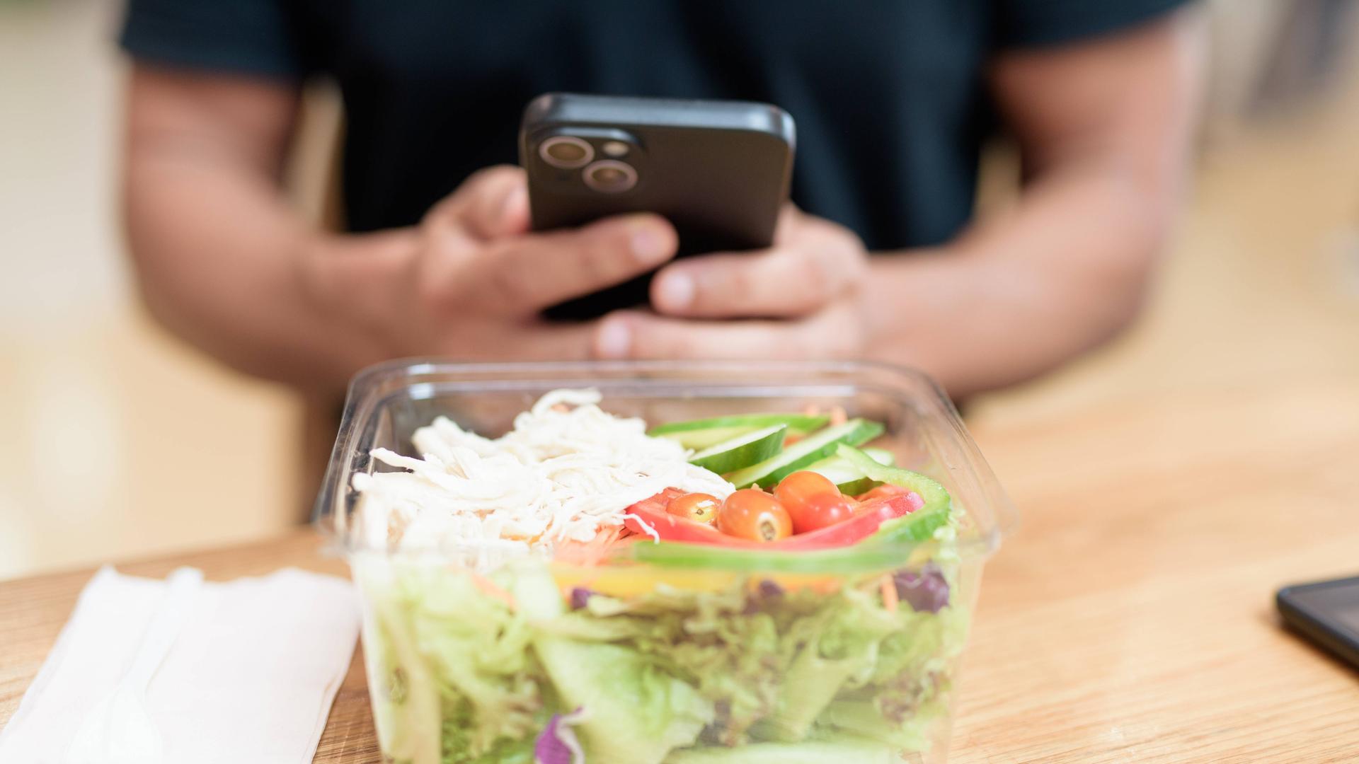 Mann mit Smartphone sitzt vor einer Salatschüssel