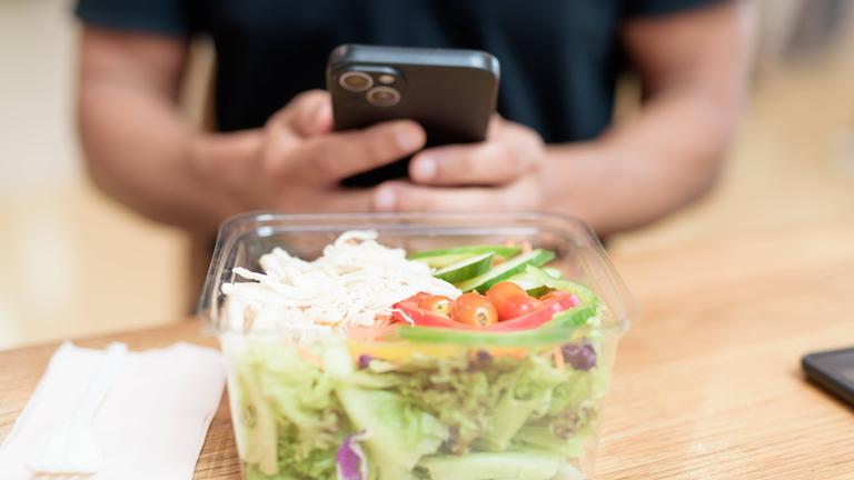 Mann mit Smartphone sitzt vor einer Salatschüssel