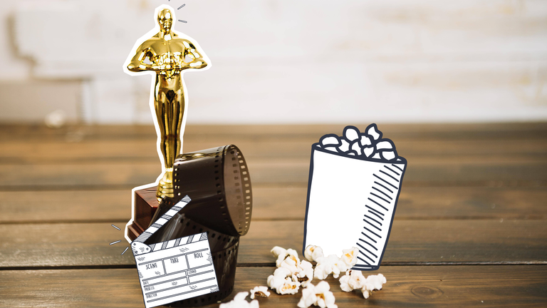 Man sieht einen Oscar, der auf einem Holzboden steht. Davor liegt eine Filmrolle. Neben dem Oscar liegt Popcorn. 