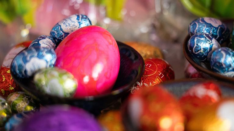 Ostereier und Schokoeier liegen in Schalen und auf einem Tisch.