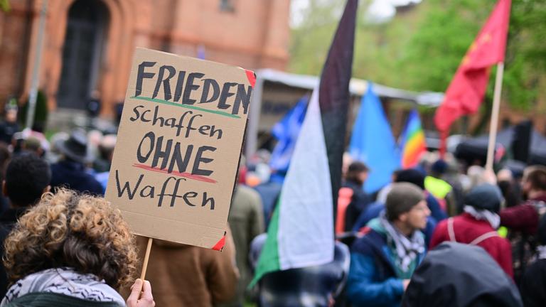 19.04.2025, Berlin: Eine Frau hält während des Abschluss des Ostermarschs 2025 ein Schild mit der Aufschrift «Frieden schaffen ohne Waffen» hoch.