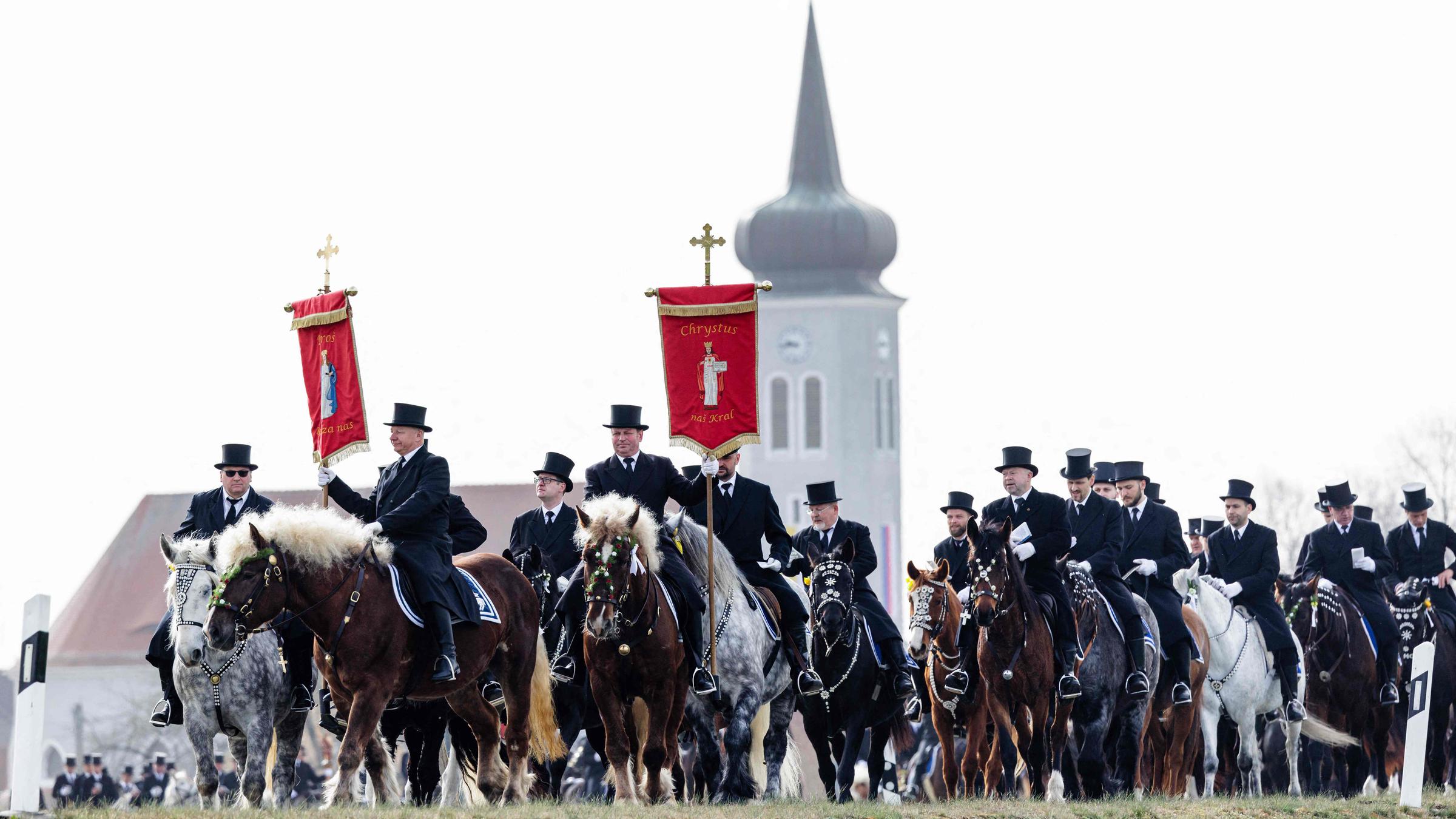 Sorbische Reiter in schwarzer Tracht singen, während sie während der sorbischen Osterprozession am Ostersonntag, dem 31.03.2024, in Ralbitz, Ostdeutschland, reiten.