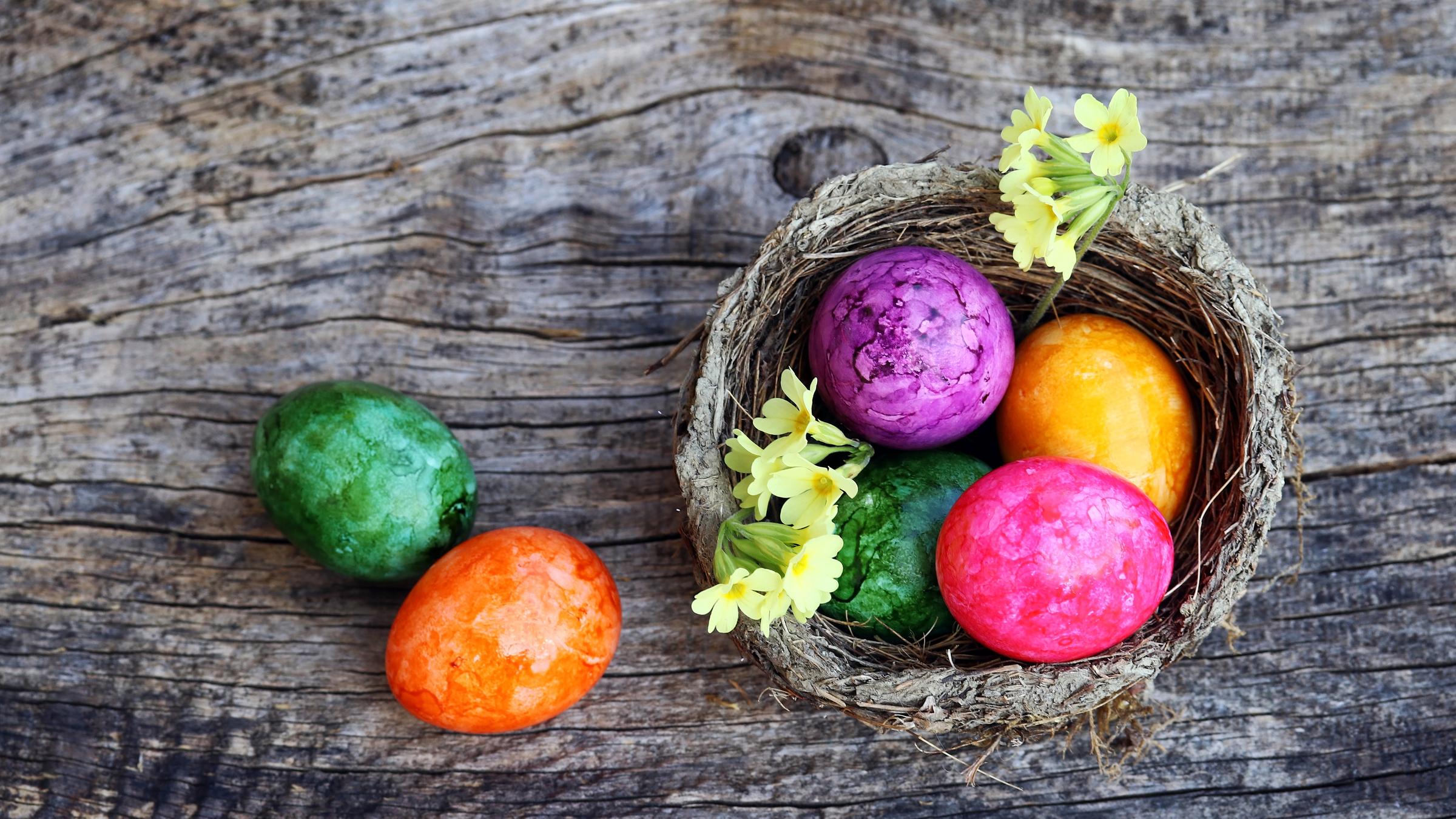 Bunte Ostereier in einem Körbchen, zwei liegen auf dem Tisch daneben.