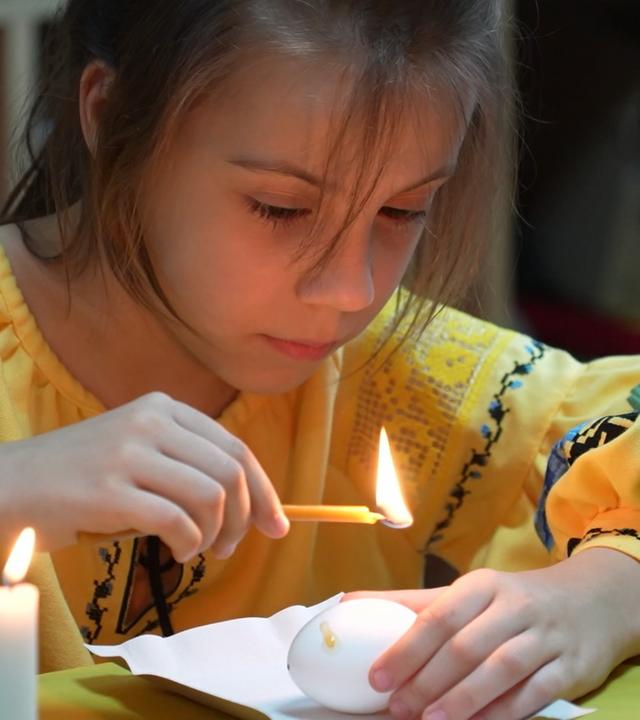 Ein Mädchen im gelben Oberteil zündet eine Kerze an 