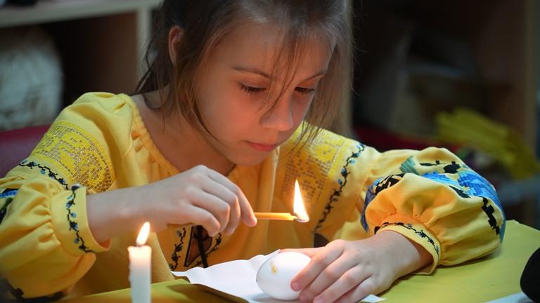 Ein Mädchen im gelben Oberteil zündet eine Kerze an 