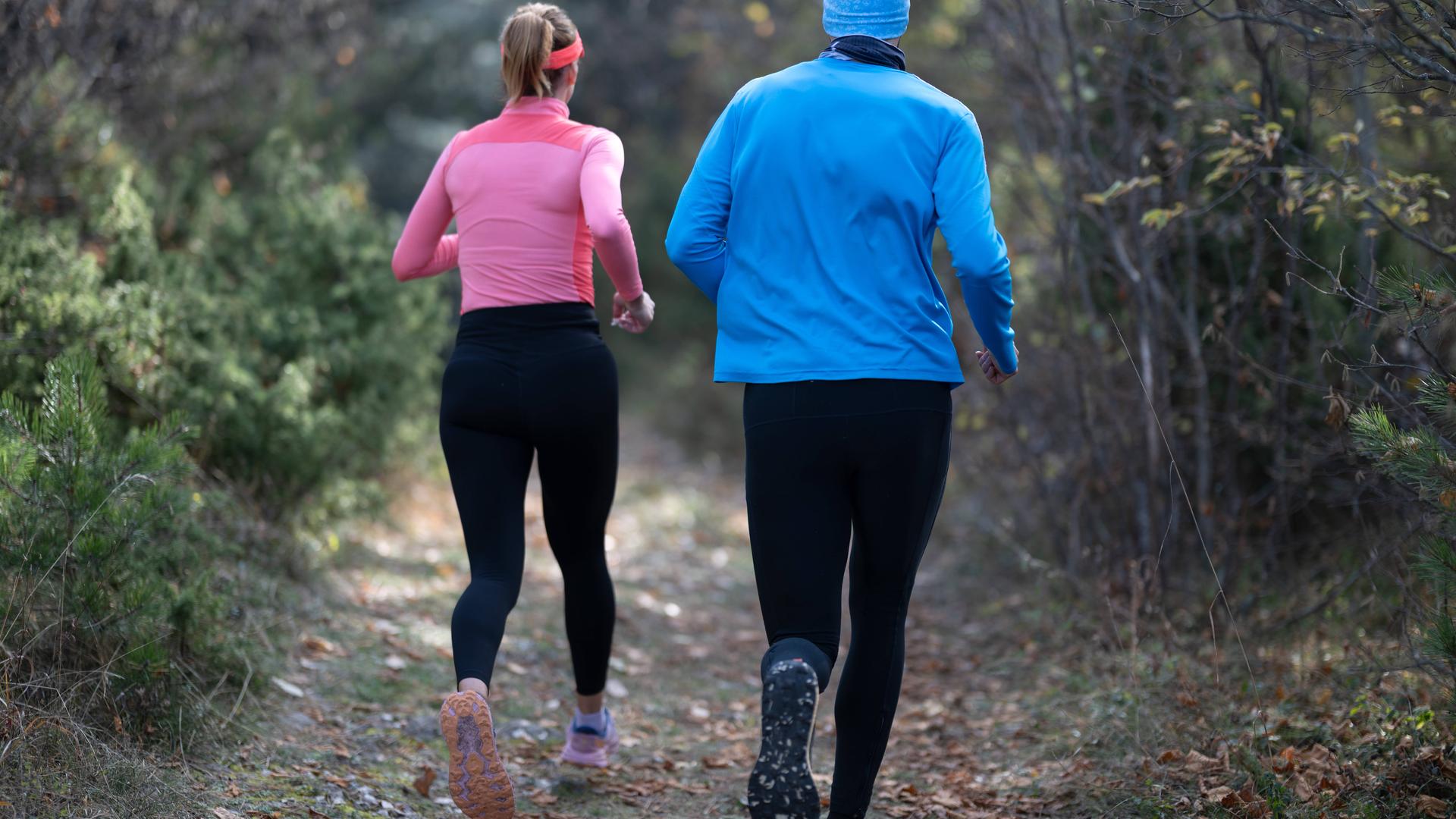 Ein sportliches Paar in Funktionskleidung joggt durch einen Wald.