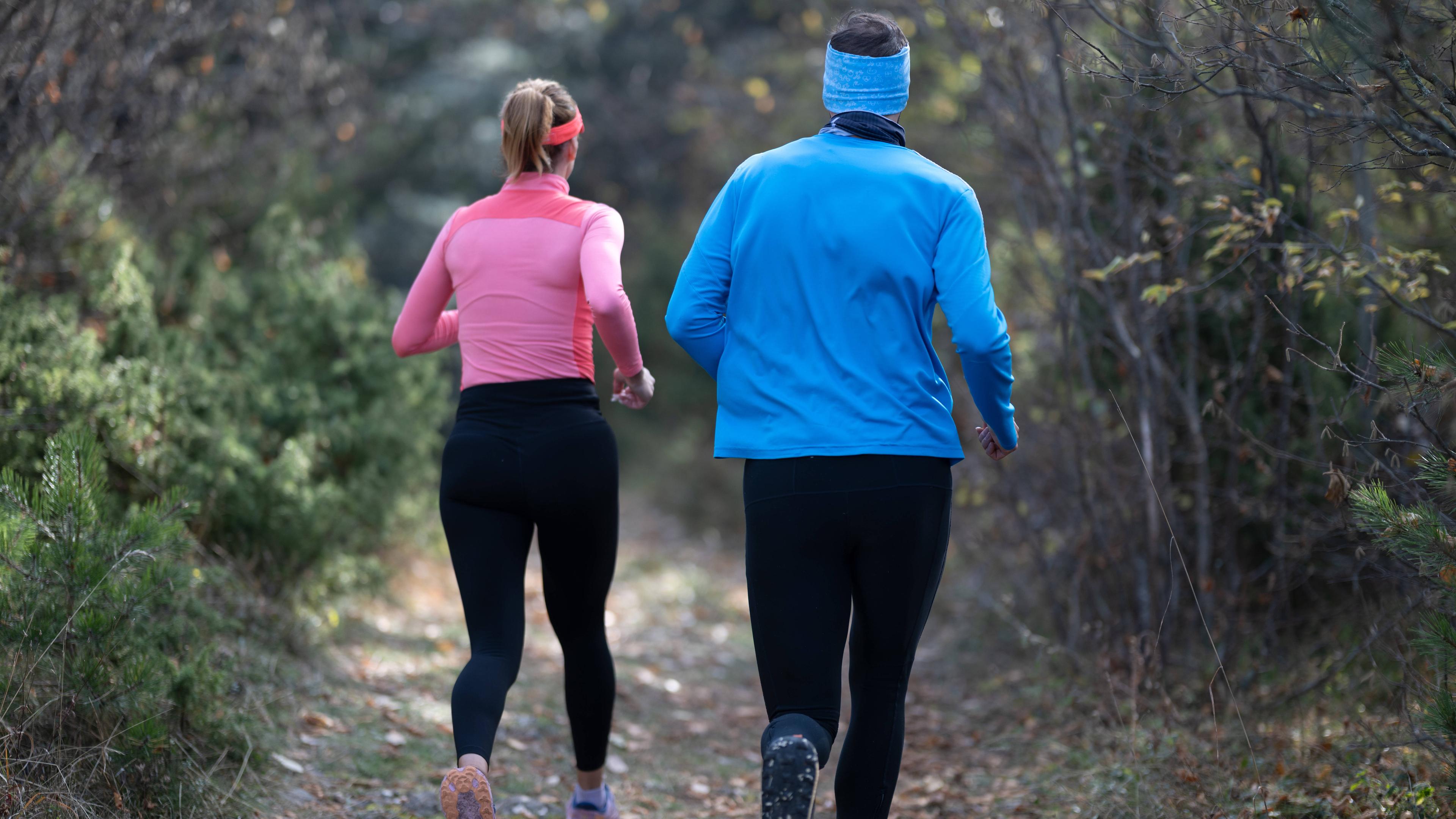 Ein sportliches Paar in Funktionskleidung joggt durch einen Wald.