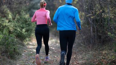 Ein sportliches Paar in Funktionskleidung joggt durch einen Wald.