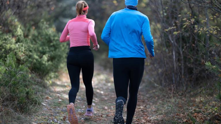 Ein sportliches Paar in Funktionskleidung joggt durch einen Wald.