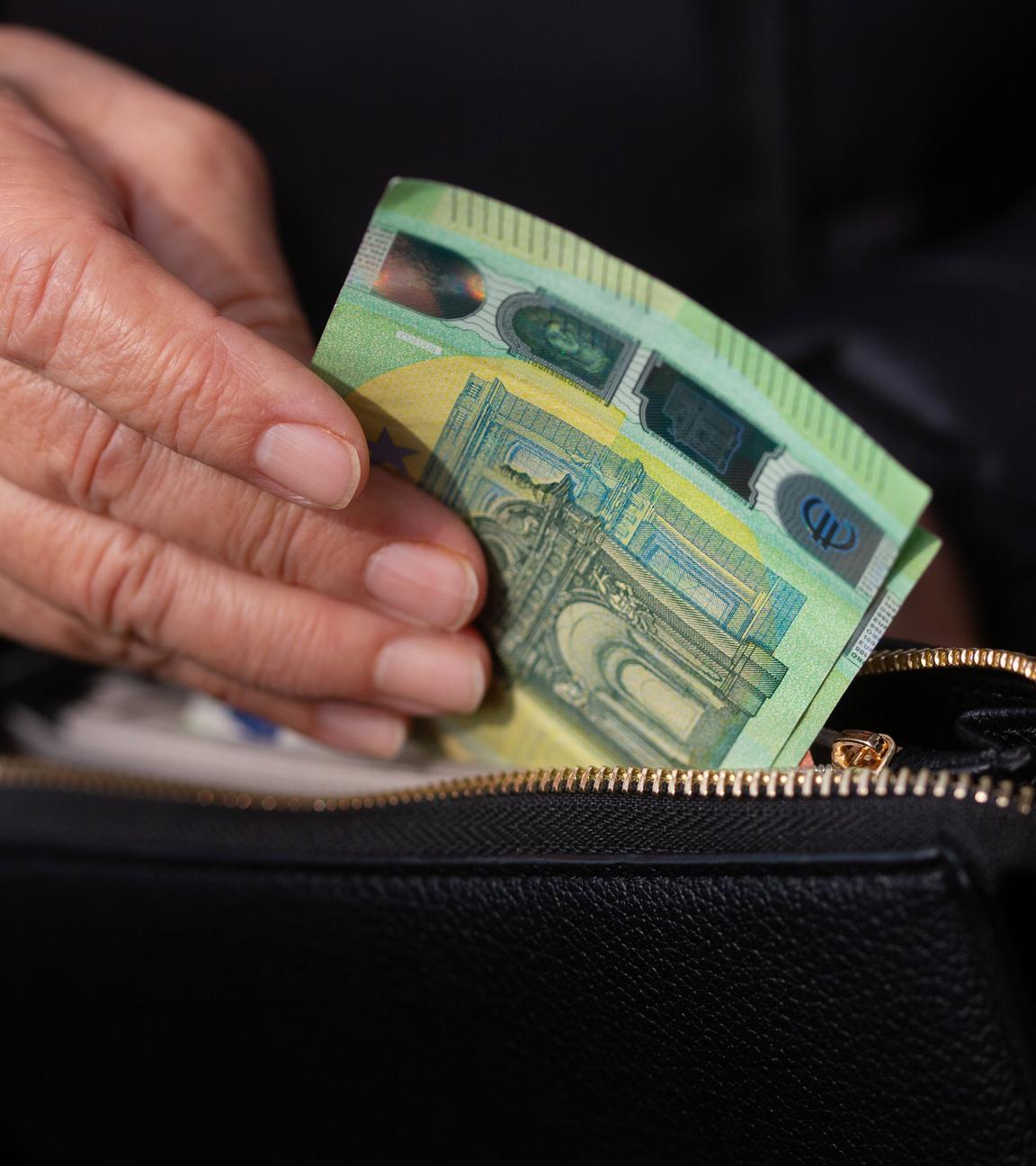 Eine Seniorin steckt Euro-Banknoten in eine Geldbörse. 