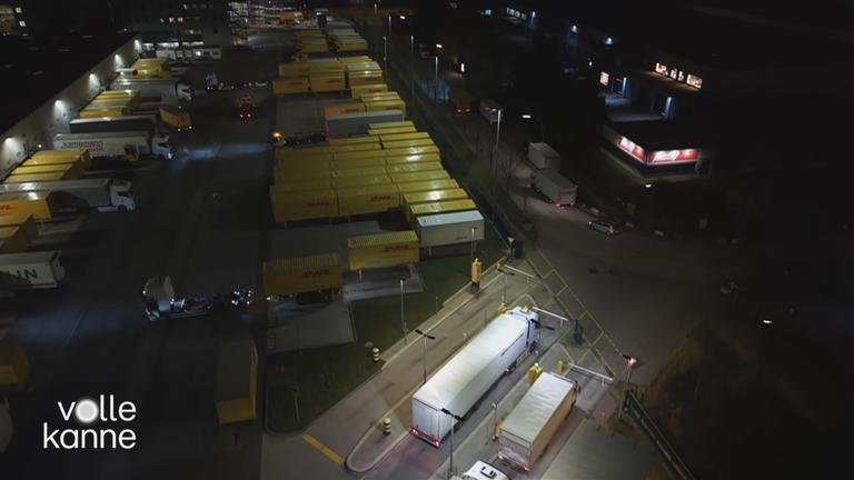 Der Parkplatz eines Paketzentrums ist zu sehen. Der Parkplatz ist voll mit LKWs. 