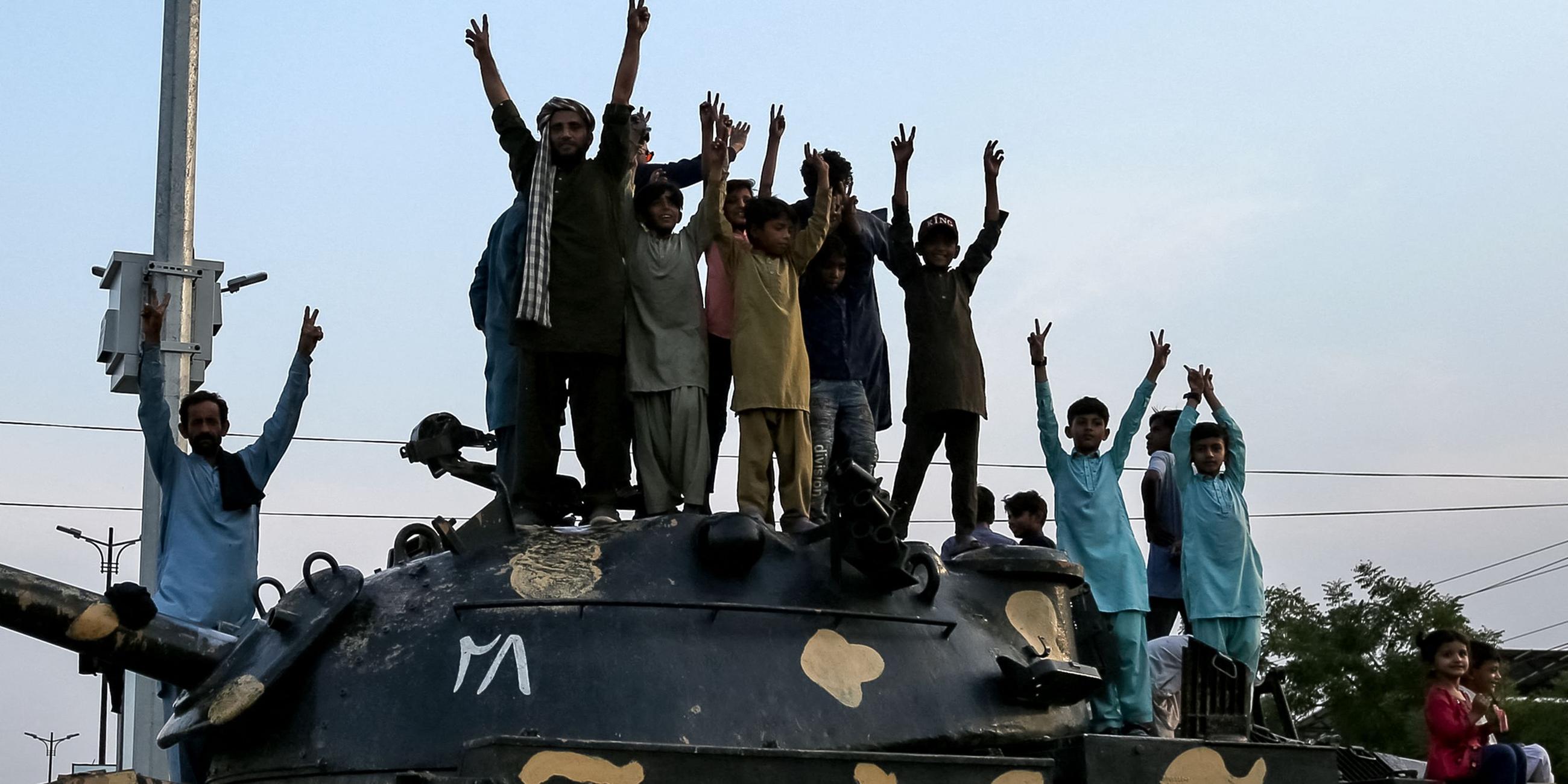 Mehrere Menschen stehen in Pakistan auf einem Panzer und strecken das Victory-Zeichen mit den Händen in die Luft, nachdem ein Waffenstillstand bekannt gegeben wurde.