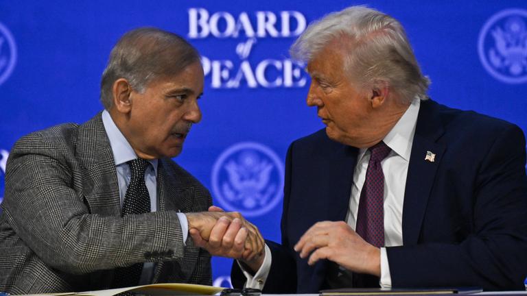 Donald Trump und Shebaz Sharif reichen sich die Hände vor blauem Hintergrund.