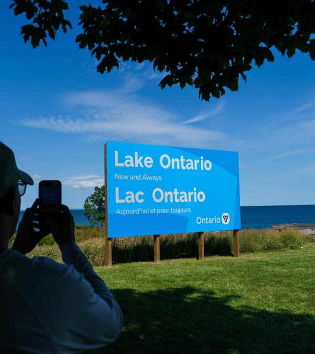 Eine Person fotografiert das neu enthüllte Schild für den Ontariosee in der Fifty Point Conservation Area. 