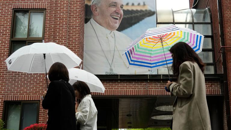 Südkorea, Seoul: Menschen gehen an einem lachenden Porträt von Papst Franziskus an der Myeongdong-Kathedrale in Seoul vorbei.