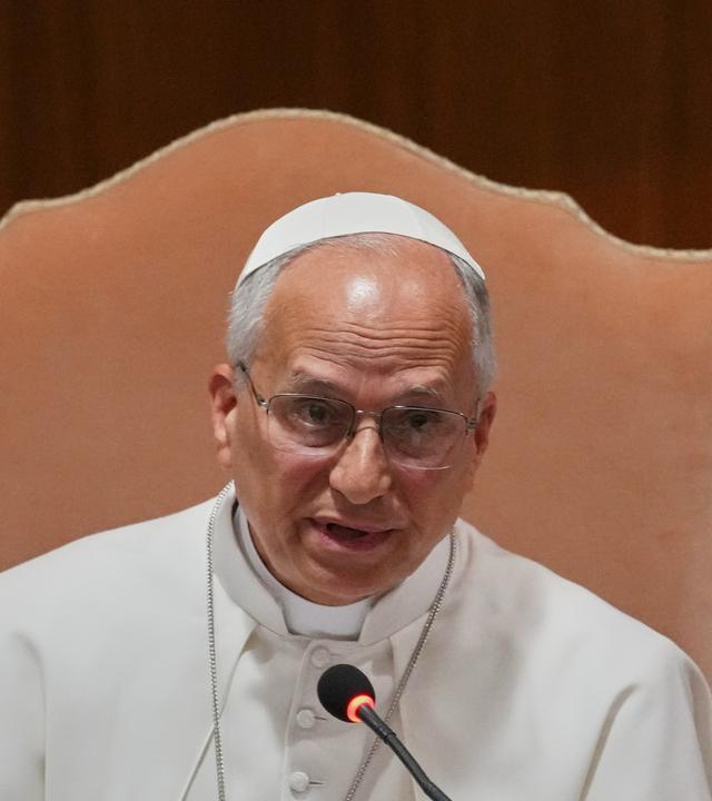 Papst Leo auf einem Stuhl vor einem Mikrofon.