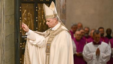 Papst Leo XIV. in päpstlichem Gewand an der Heiligen Pforte des Petersdoms. Im Hintergrund mehrere andere Priester/Kardinäle.