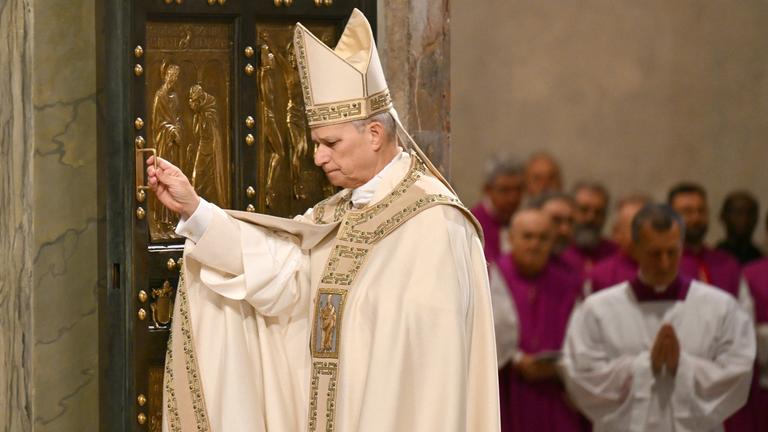 Papst Leo XIV. in päpstlichem Gewand an der Heiligen Pforte des Petersdoms. Im Hintergrund mehrere andere Priester/Kardinäle.