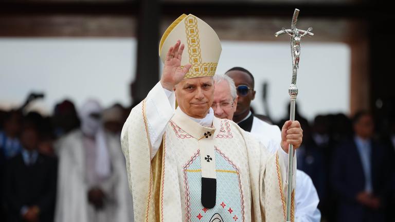 Papst Leo in weißem Gewand, winkt mit der linken Hand.