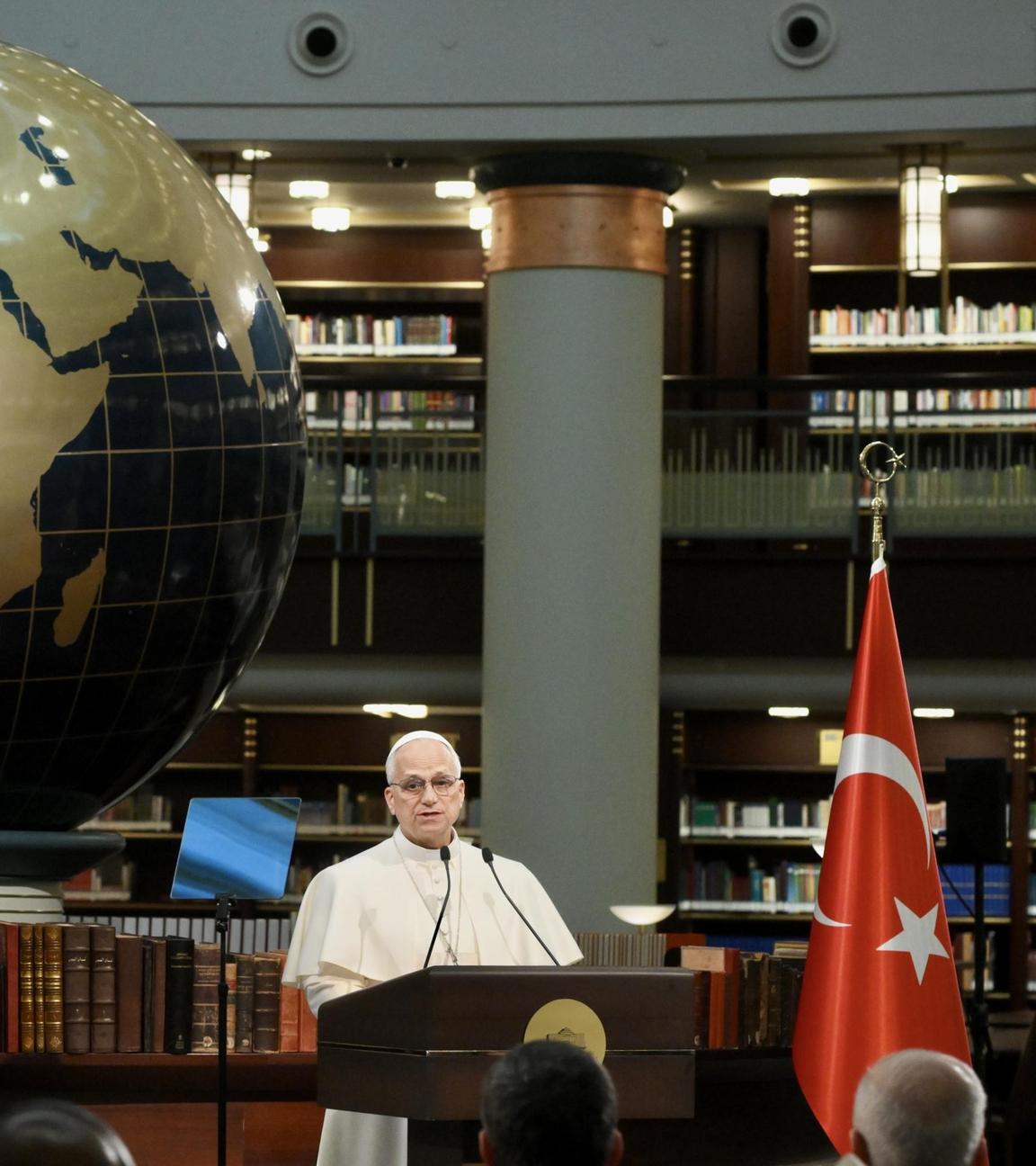 Papst Leo XIV. hält vor einer großen Weltkugel eine Rede.