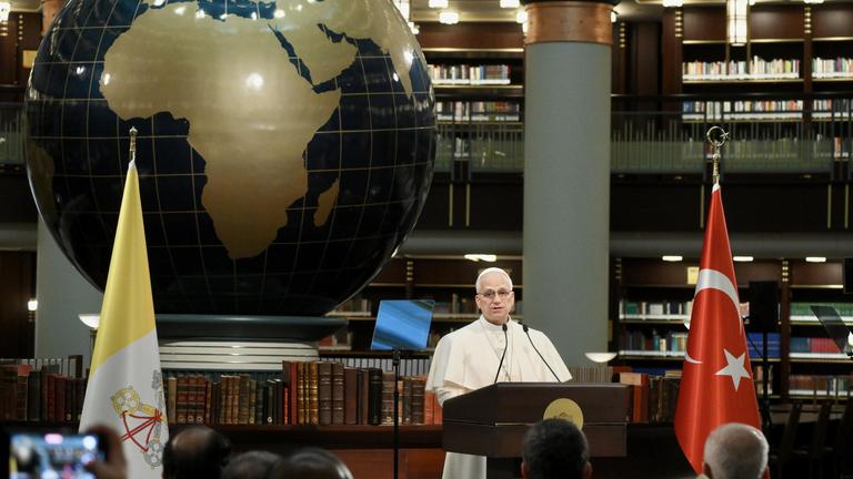 Papst Leo XIV. hält vor einer großen Weltkugel eine Rede.