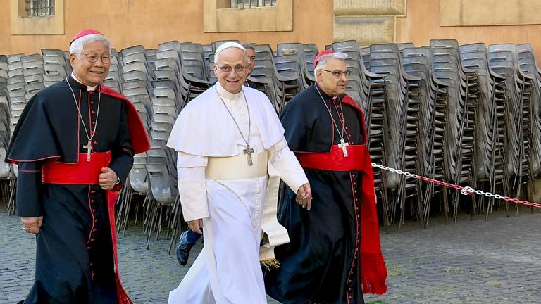 Papst Leo XIV. läuft mit zwei Kardinälen durch die Straßen des Vatikans.