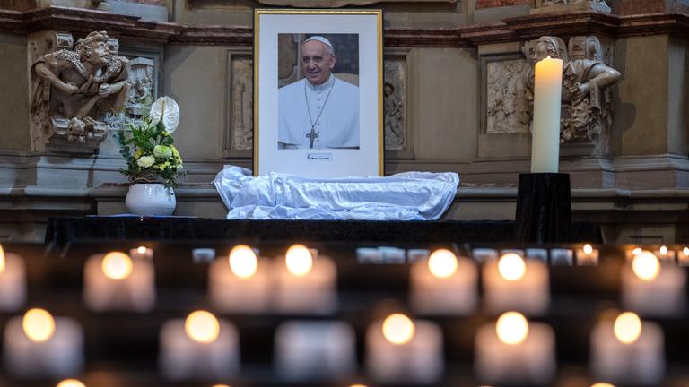 Ein Bild des verstorbenen Papst Franziskus, im Vordergund sind einige Kerzen zu sehen