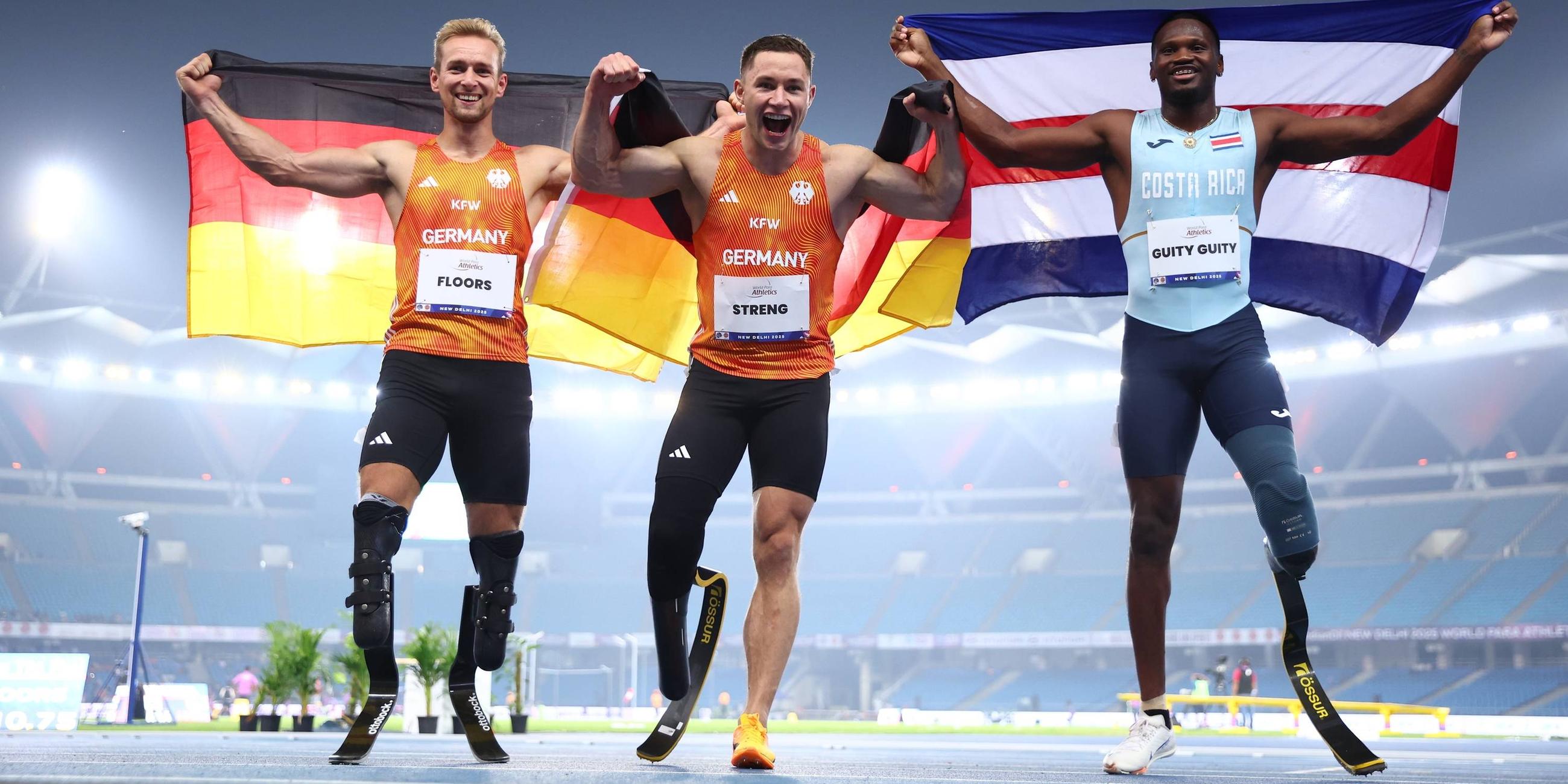 Johannes Floors und Felix Streng (Team Deutschland) sowie Sherman Guity Guity (Costa Rica) nach dem 100-Meter-Finale (T64) bei der Para-WM in Neu-Delhi am 30.09.2025.