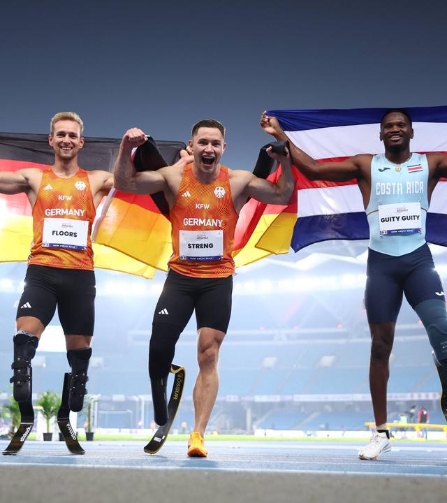 Johannes Floors und Felix Streng (Team Deutschland) sowie Sherman Guity Guity (Costa Rica) nach dem 100-Meter-Finale (T64) bei der Para-WM in Neu-Delhi am 30.09.2025.