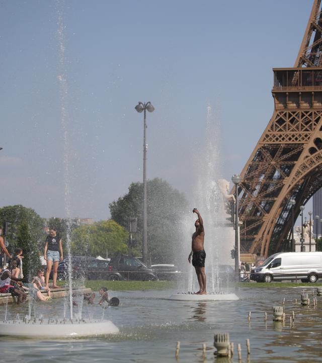 Ein Mann steht in Badehosen im Trocadero-Brunnen in Paris nahe dem Eiffelturm. 