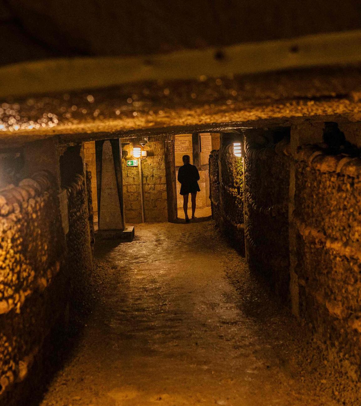 Eine Touristin betrachtet am 12. August 2025 in den Katakomben von Paris menschliche Schädel und Knochen, die aus überfüllten Pariser Friedhöfen dorthin verlegt wurden.