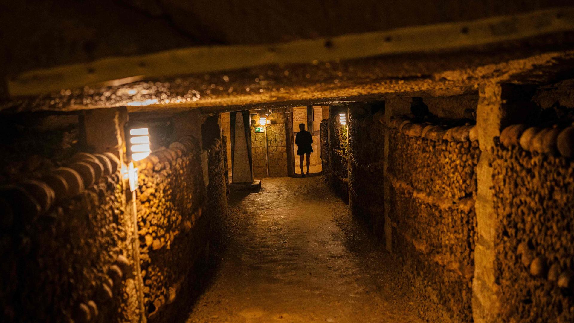 Eine Touristin betrachtet am 12. August 2025 in den Katakomben von Paris menschliche Schädel und Knochen, die aus überfüllten Pariser Friedhöfen dorthin verlegt wurden.