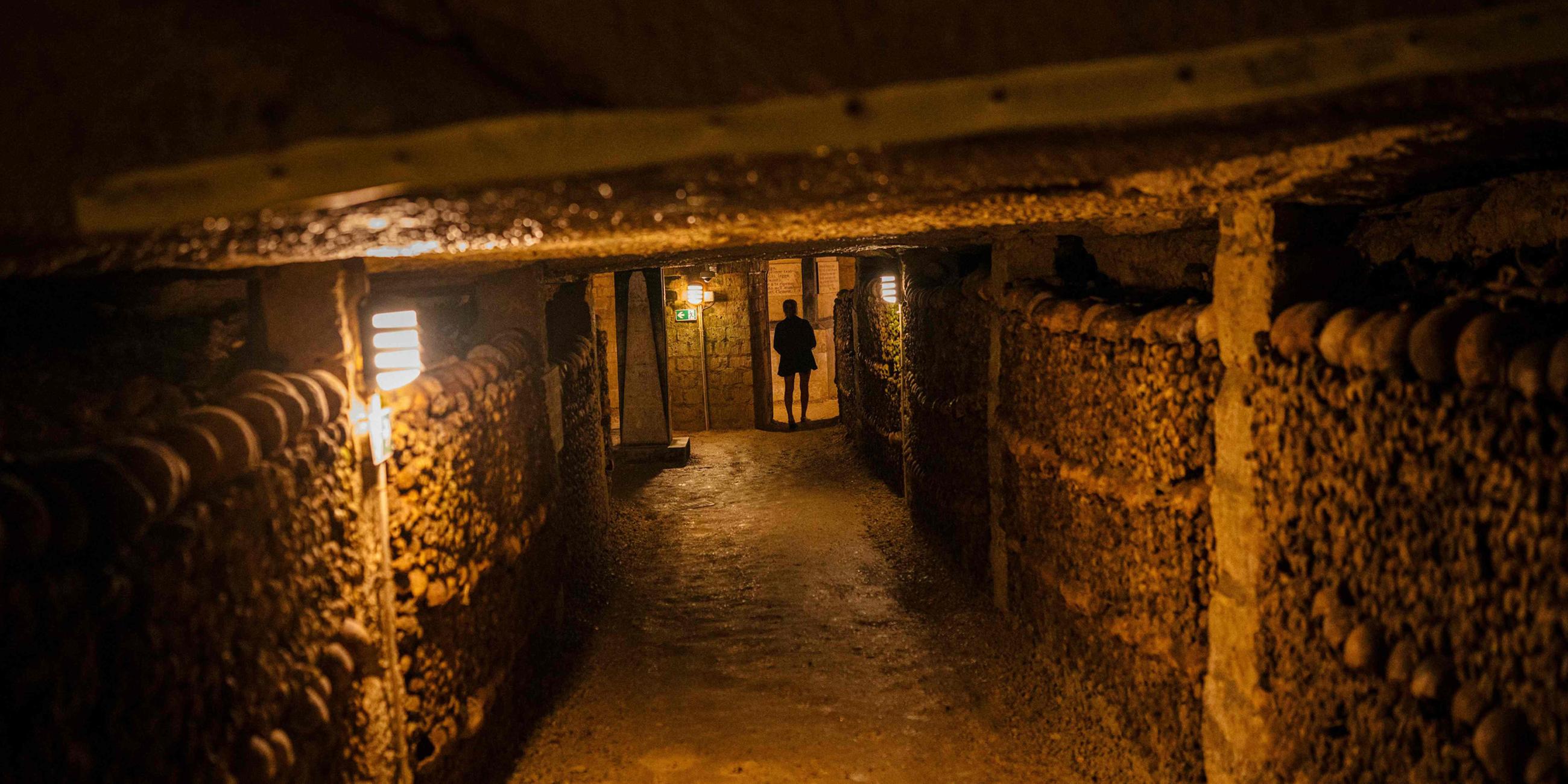 Eine Touristin betrachtet am 12. August 2025 in den Katakomben von Paris menschliche Schädel und Knochen, die aus überfüllten Pariser Friedhöfen dorthin verlegt wurden.