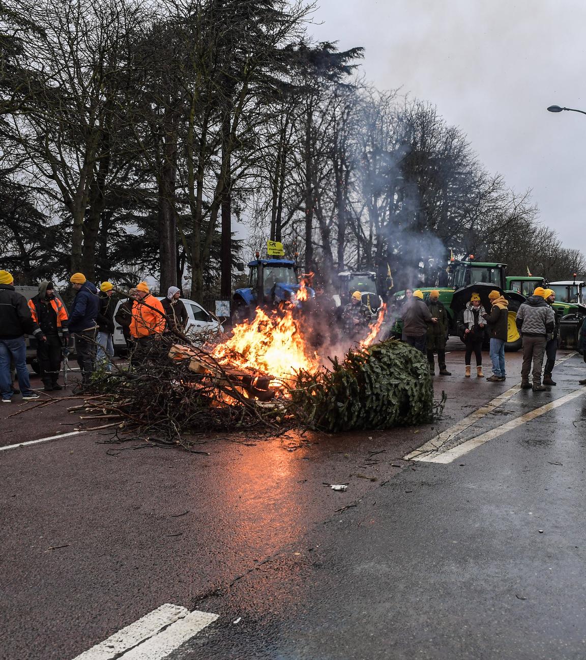 Landwirte aus Paris protestieren auf der Staße mit ihren Traktoren. Mitten auf der Straße liegt ein brennender Baum.