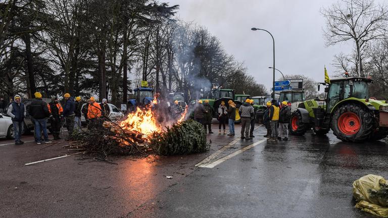 Landwirte aus Paris protestieren auf der Staße mit ihren Traktoren. Mitten auf der Straße liegt ein brennender Baum.
