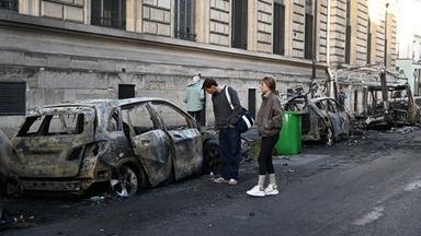 Menschen schauen sich nach den Protesten die verbrannten Überreste von Autos in der Nähe des Platzes der Republik in Paris an.