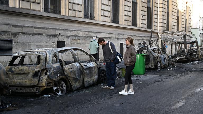 Menschen schauen sich nach den Protesten die verbrannten Überreste von Autos in der Nähe des Platzes der Republik in Paris an.