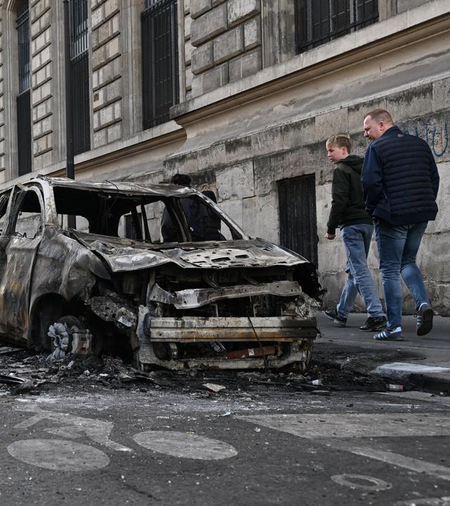 Menschen schauen sich nach den Protesten die verbrannten Überreste von Autos in der Nähe des Platzes der Republik in Paris an.