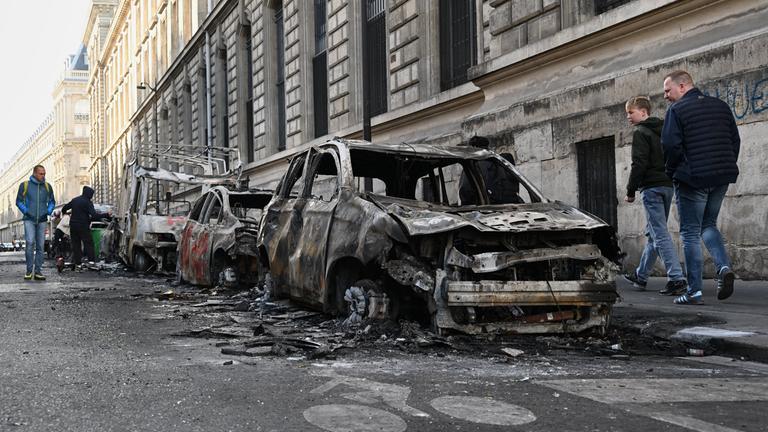 Menschen schauen sich nach den Protesten die verbrannten Überreste von Autos in der Nähe des Platzes der Republik in Paris an.