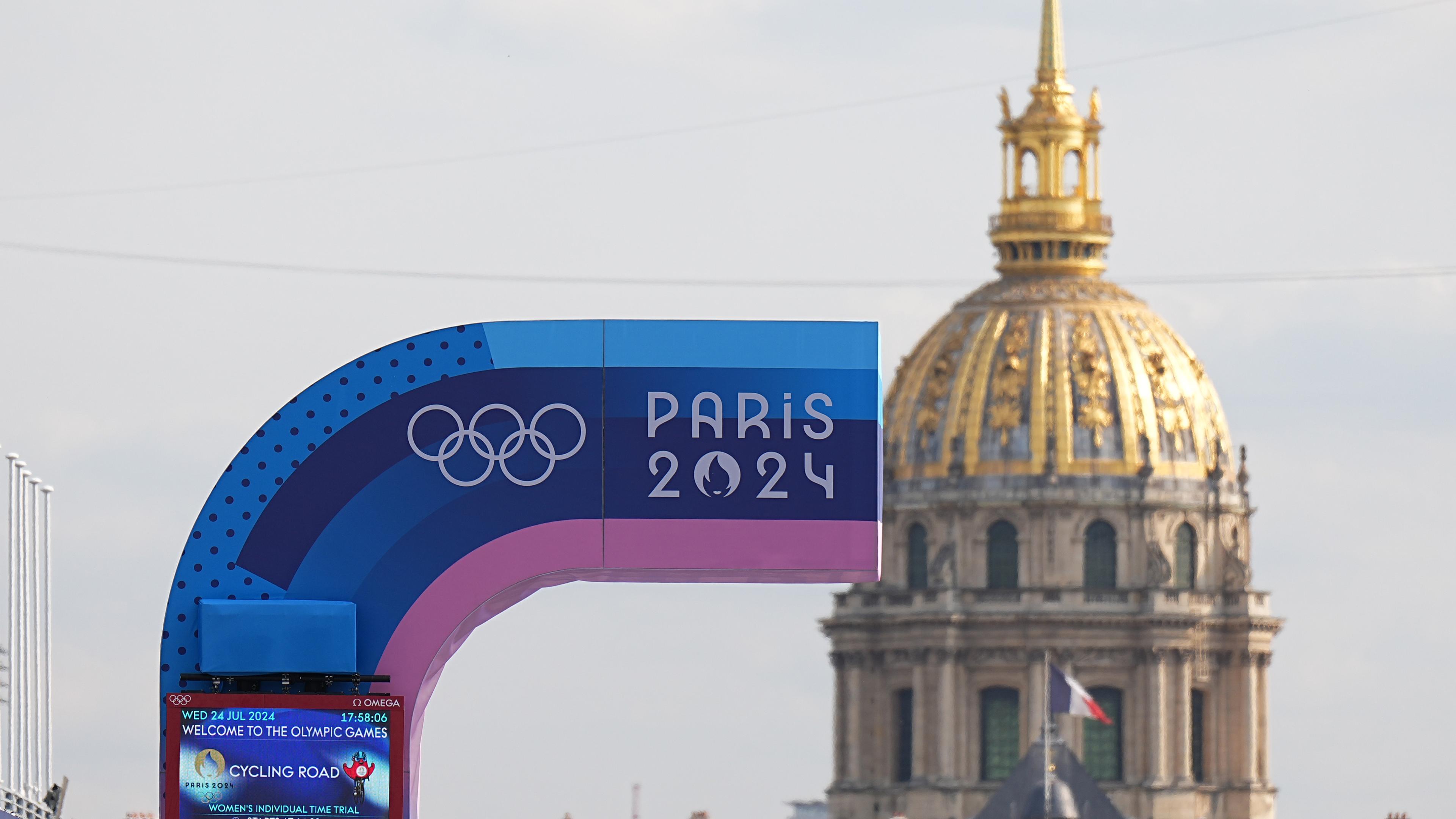 24.07.2024, Frankreich, Paris: Vor den Olympischen Sommerspielen, Olympia Paris 2024, eine Anzeigetafel und die Olympischen Ringe sind vor der Kuppel des Hotel des Invalides zu sehen.