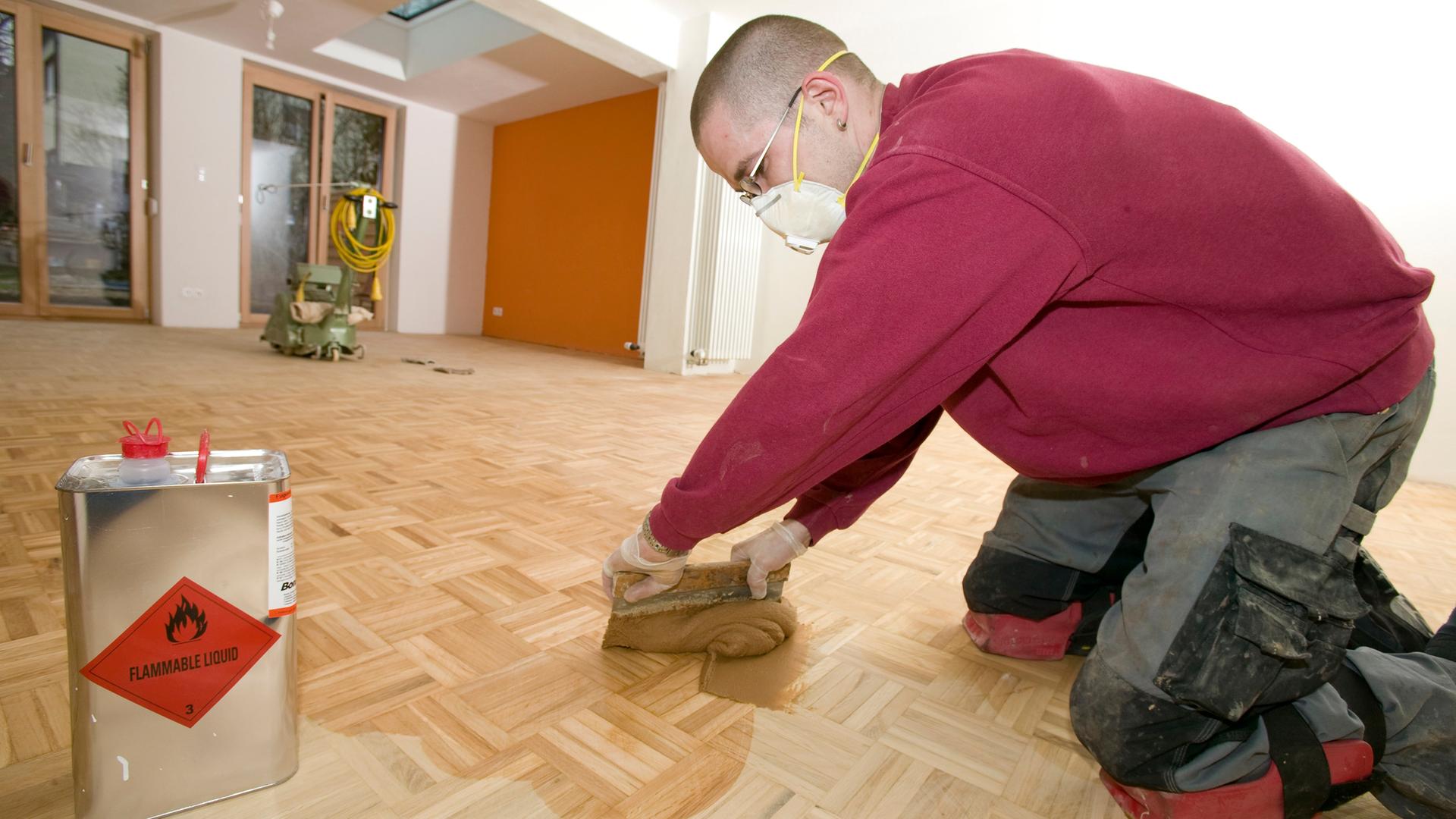 Ein Parkettleger kniet auf dem Boden und ölt das Parkett ein.