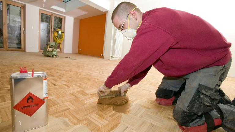 Ein Parkettleger kniet auf dem Boden und ölt das Parkett ein.