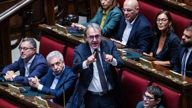 Mitglieder des italienisches Parlaments. Ein Mann steht mit erhobenen Zeigefingern an seinem Sitz.