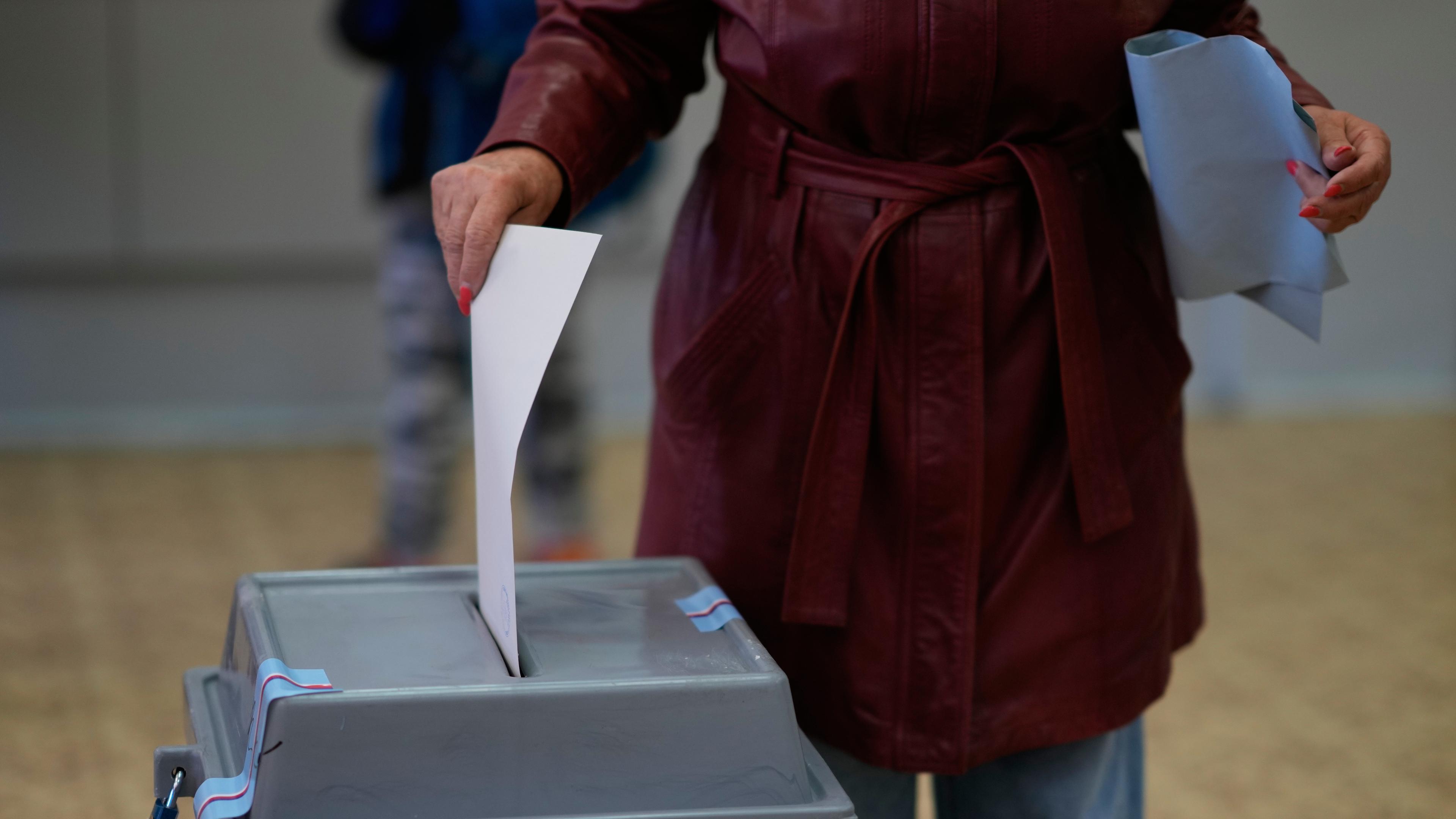 Eine Person wirft einen Wahlzettel in eine Wahlurne