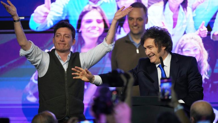 Argentinien, Buenos Aires: Der argentinische Präsident Javier Milei (r) und sein Berater Santiago Caputo winken nach Schließung der Wahllokale bei der Parlamentswahl ihren Anhängern zu.