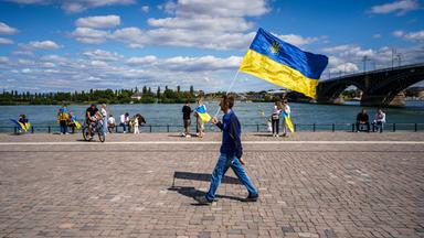 Ein Mann geht auf einer Kundgebung zum 34. Unabhängigkeitstag der Ukraine mit der ukrainischen Nationalflagge am Rheinufer.