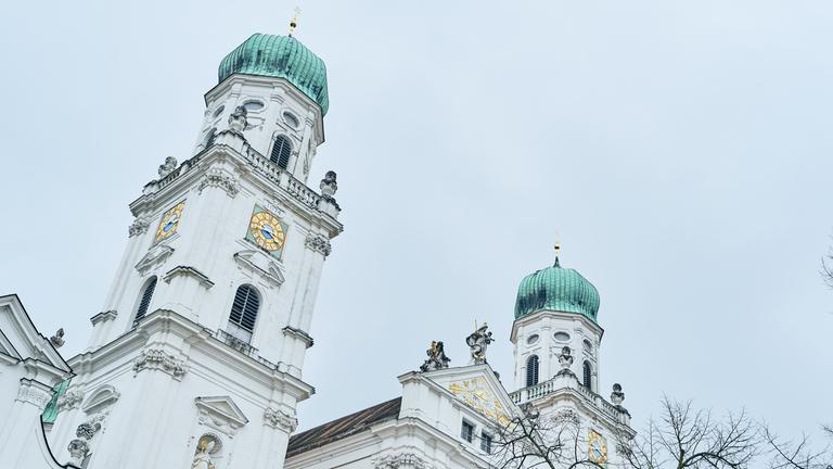 Die weißen Türme des Passauer Doms mit grüner Spitze vor grauem Himmel