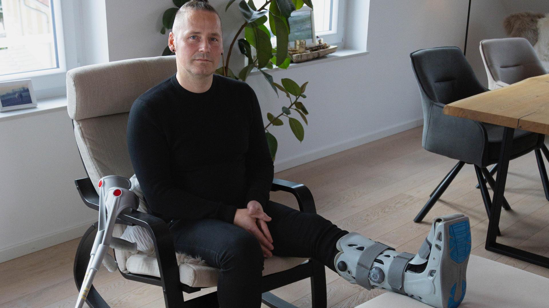 Der Patient Thomas Gölkel sitzt auf einem Sessel mit einer Beinschiene am linken Bein. 