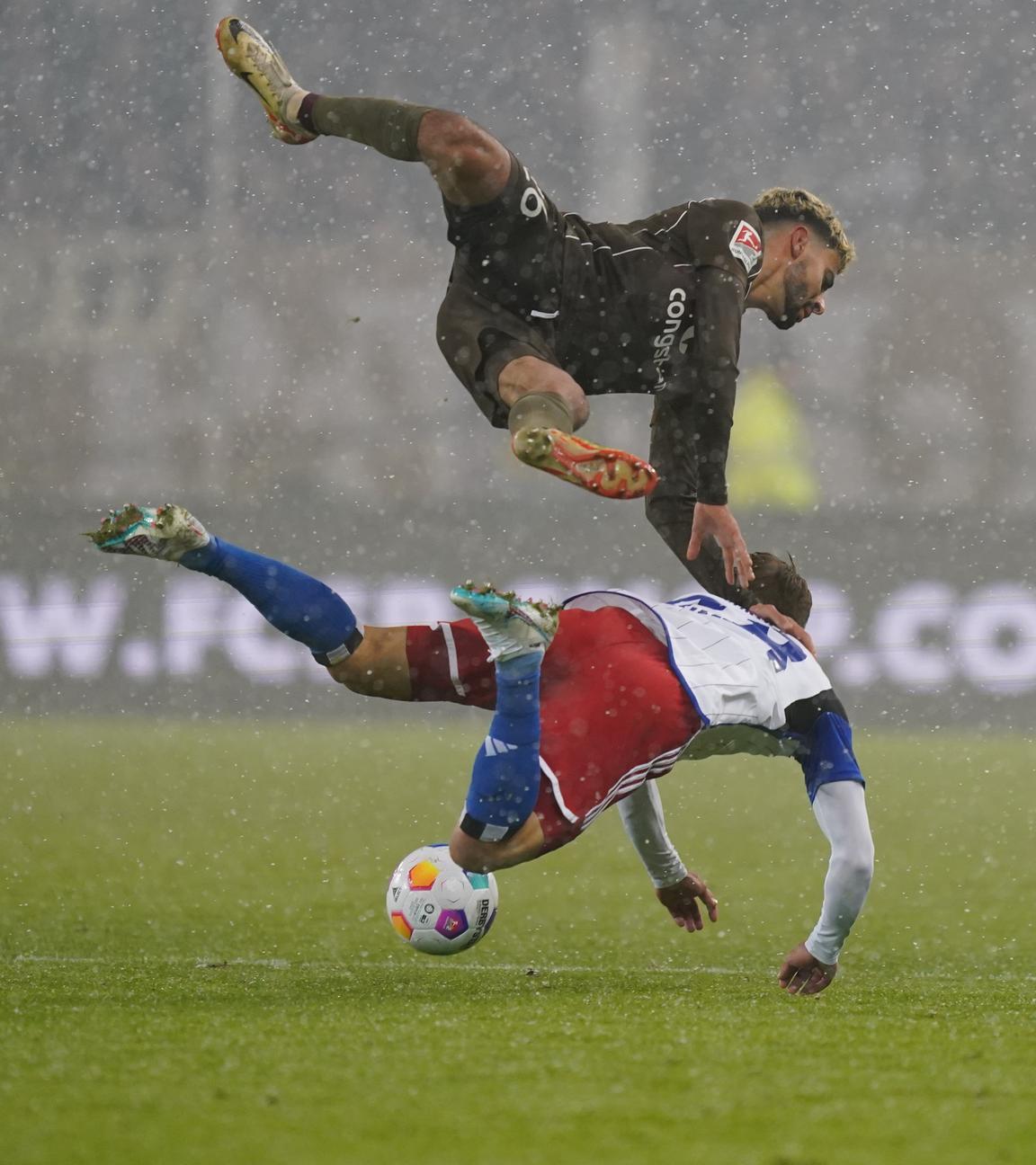 Miro Muheim vom HSV und St. Paulis Elias Saad fallen beim Spiel am 01.12.2023 im Zweikampf zu Boden.